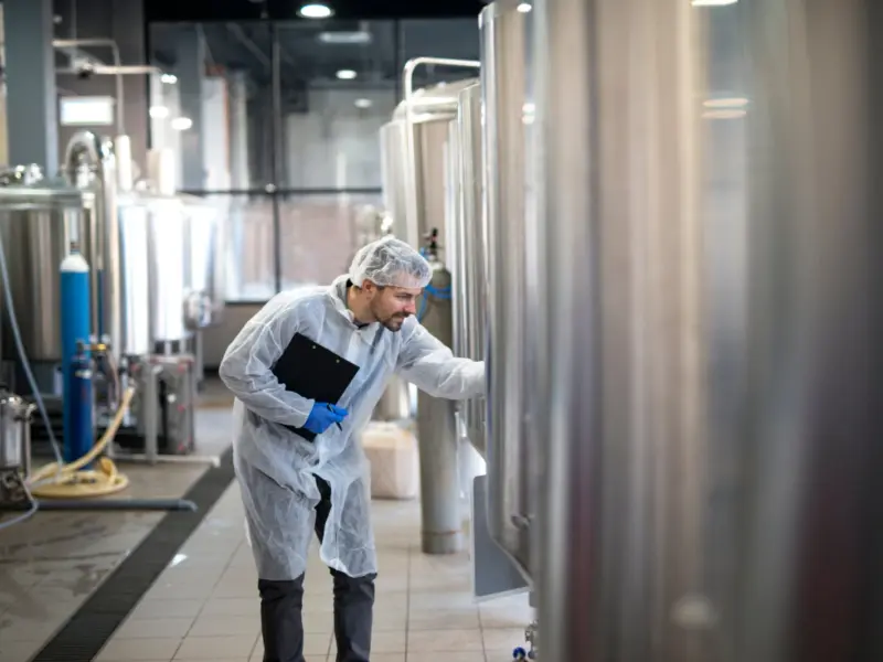 Medewerker inspecteert tanks in een voedingsfabriek